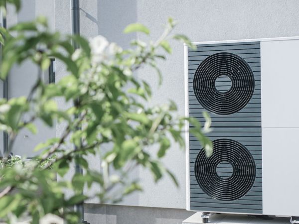 Wärmepumpe steht vor einer Hauswand.